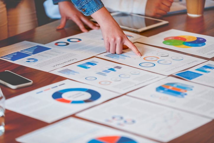 Graphs and charts printed on a boardroom table being reviewed by marketing professionals.